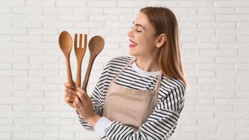 Žena v kuchynskej zástere drží v rukách drevené varechy a usmieva sa