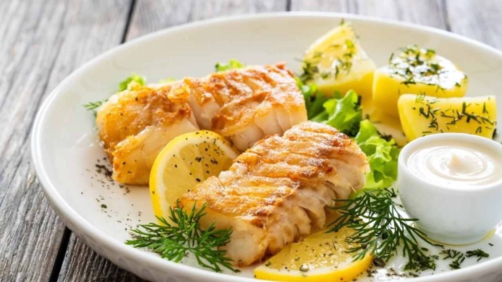 Opečené filé z tresky tmavej s citrónom, zemiakmi a bylinkami na tanieri