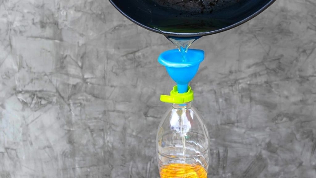 Prelievanie vychladnutého použitého oleja z panvice cez lievik do plastovej fľaše.