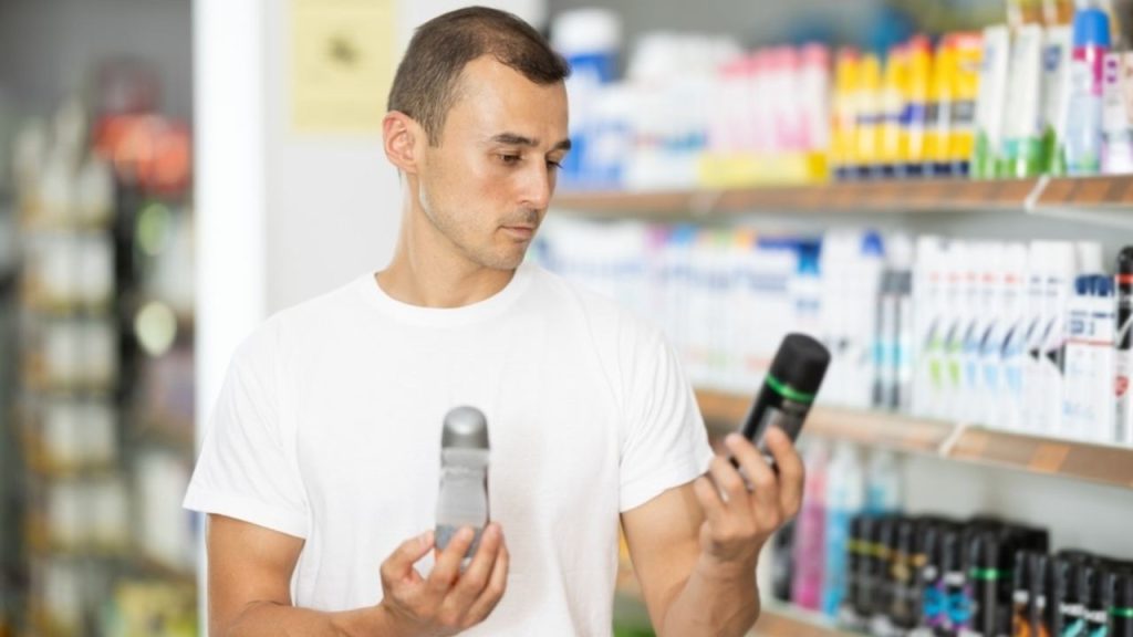 Muž v obchode porovnáva dezodorant a antiperspirant pri výbere správneho produktu.
