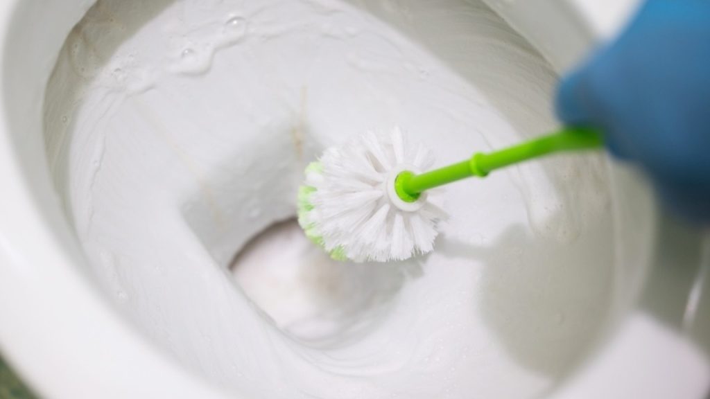 Čistenie toalety penou na holenie pomocou WC kefy v rukavici.