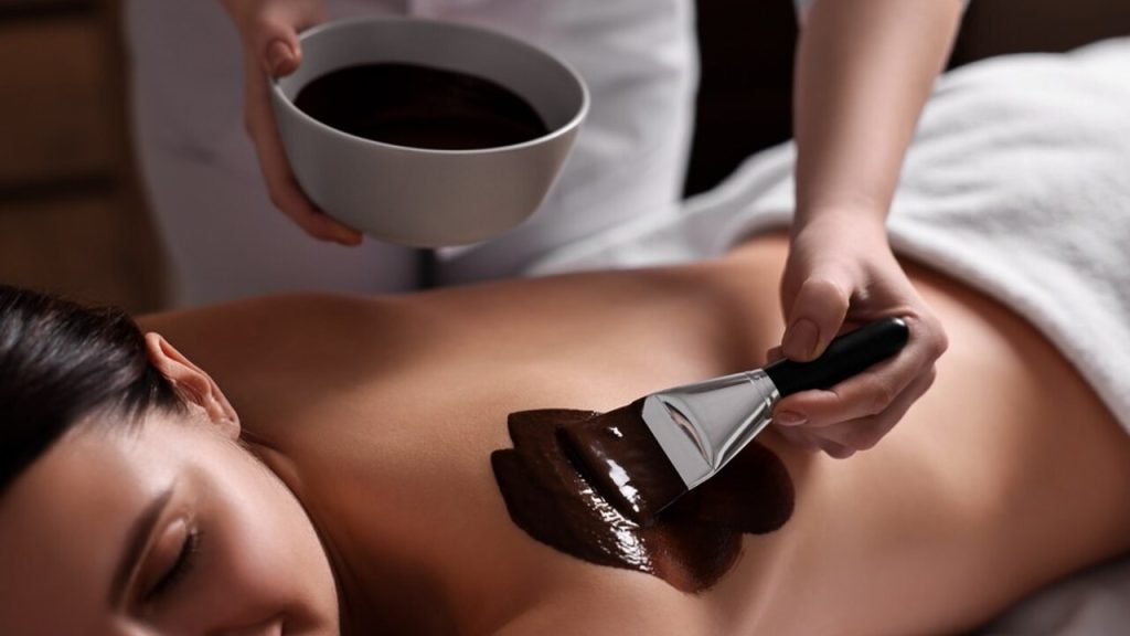 Kakaový telový zábal nanášaný štetcom počas relaxačného spa rituálu.