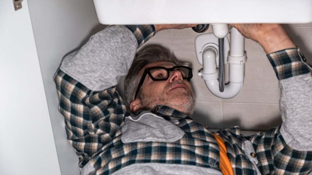 Inštalatér pracuje pod drezom a kontroluje potrubie, aby odstránil upchatie.