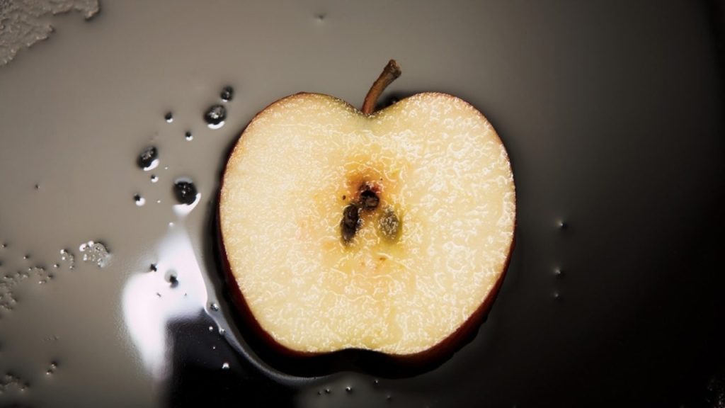 Rozkrojené surové jablko položené na tmavom povrchu ako domáci trik proti zápachu pri vyprážaní ryby