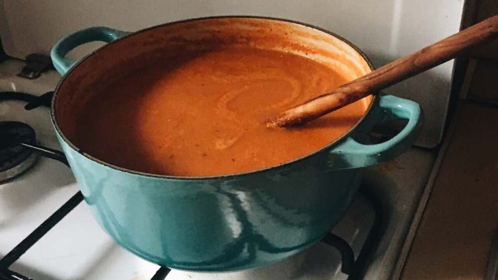 Drevená varecha ponorená v hrnci s horúcou omáčkou na sporáku