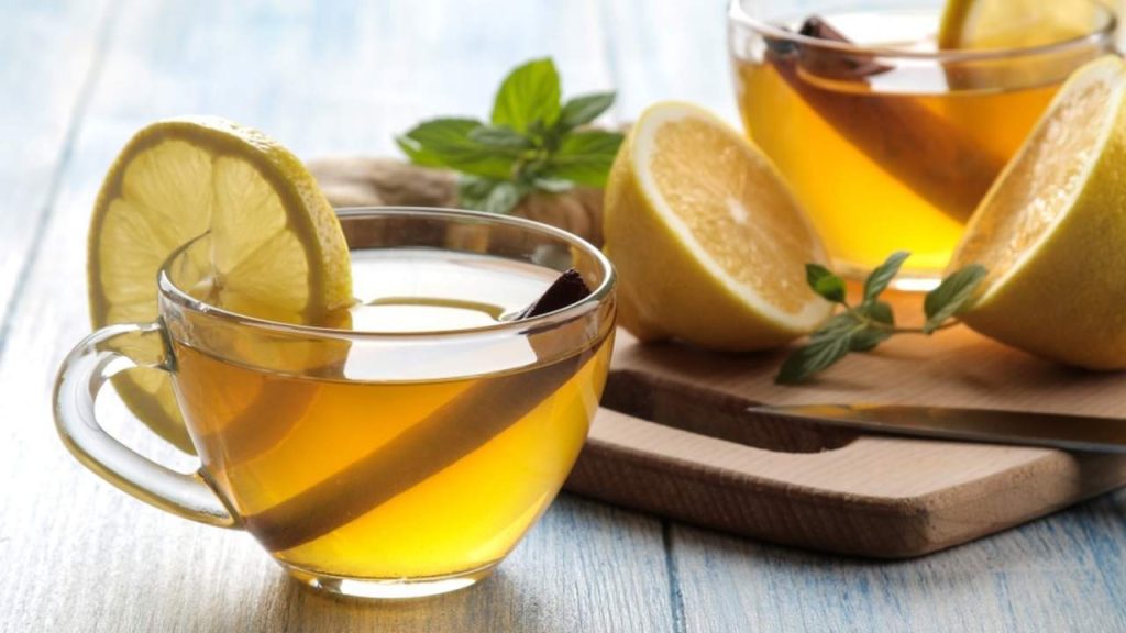 Šálka bylinkového čaju s citrónom, škoricou, zázvorom a mätou na drevenom stole