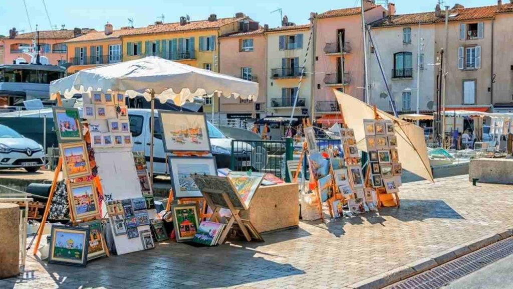 Uličný umelecký trh v prístave Saint-Tropez na Francúzskej riviére s obrazmi a farebnými domami