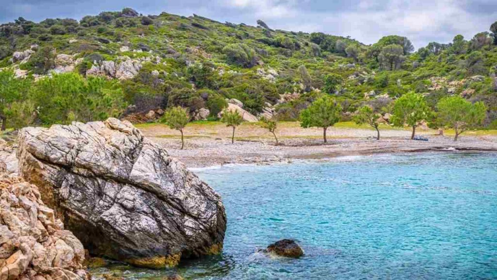 Pláž Iero, ostrov Ikaria, Grécko, zátoka s vlnami Ikarského mora, ktoré v lete omývajú pobrežné skaly pri Dionýzovom jaskynnom chráme.