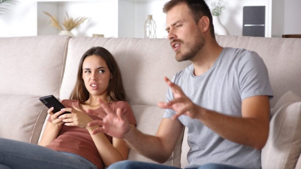 Muž gestikuluje a vysvetľuje, žena sedí na gauči a pozerá naňho s nedôverou