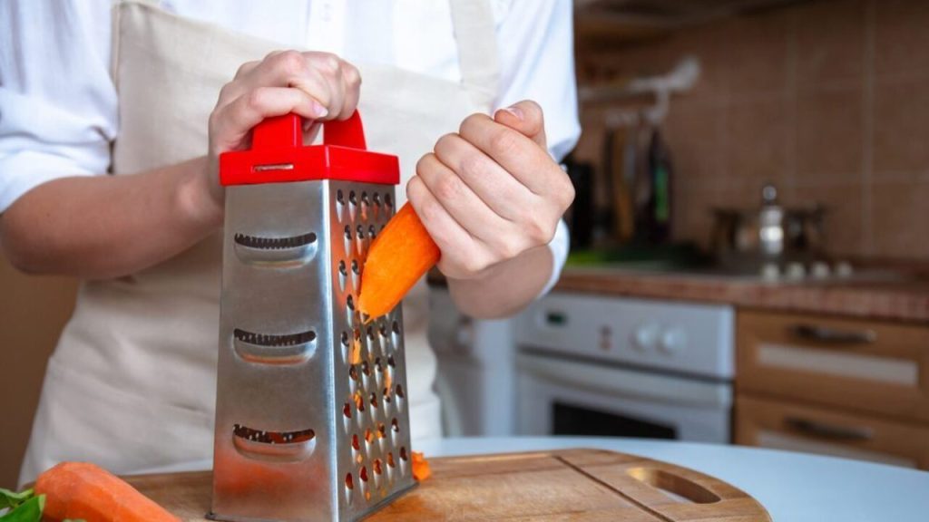 Strúhanie mrkvy na kovovom kuchynskom strúhadle na drevenej doske