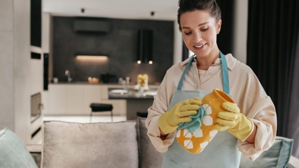 Žena v kuchyni čistí dekoratívnu keramickú vázu handričkou a má na rukách ochranné rukavice