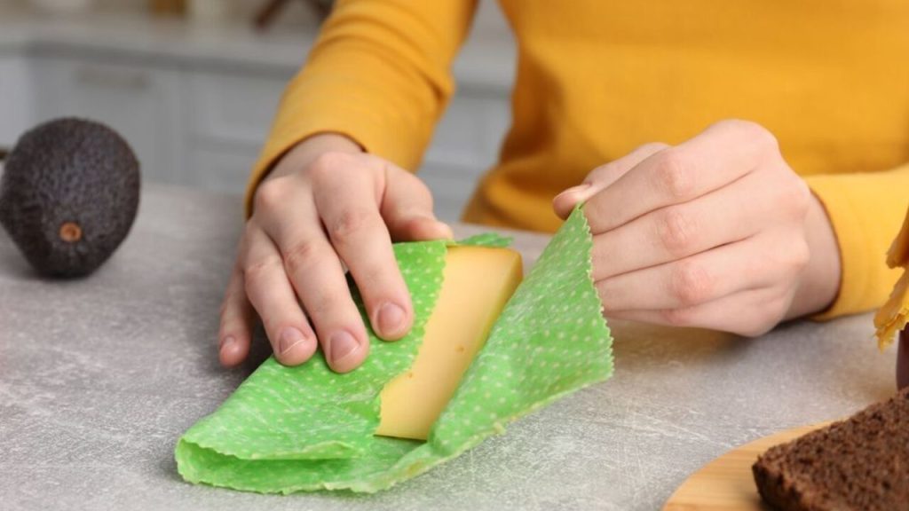 Ruky balia kúsok tvrdého syra do opakovane použiteľného voskového obrusu na kuchynskej linke