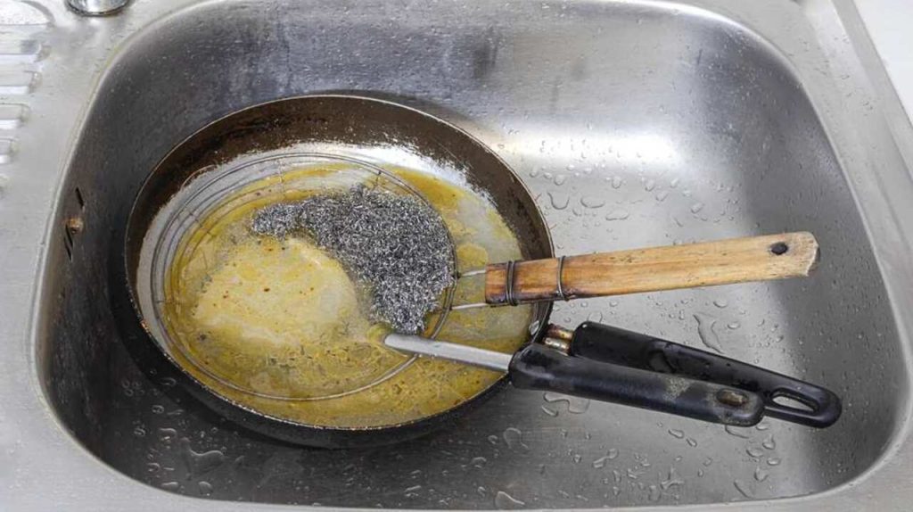 Panvica s mastným olejom a špinavým riadom v kuchynskom dreze