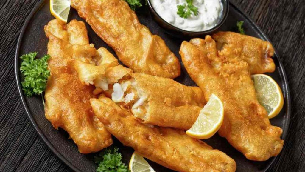 Chrumkavá ryba v pivnom cestíčku podávaná s citrónom a cesnakovým dipom na tmavom tanieri