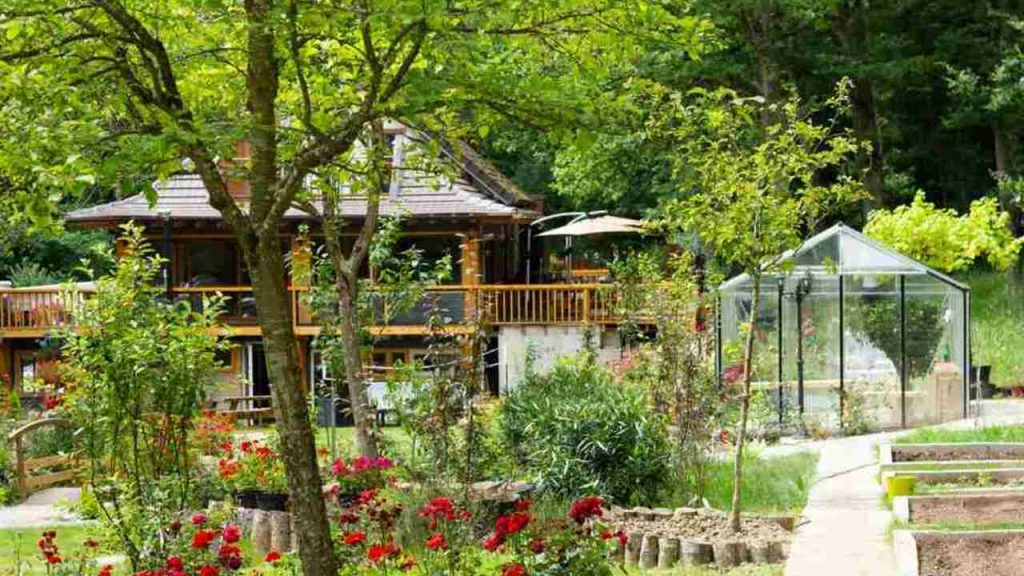 Rodinný dom so záhradou plnou stromov, kvetov a skleníkom, upravené záhony a chodníky v zelenej záhrade