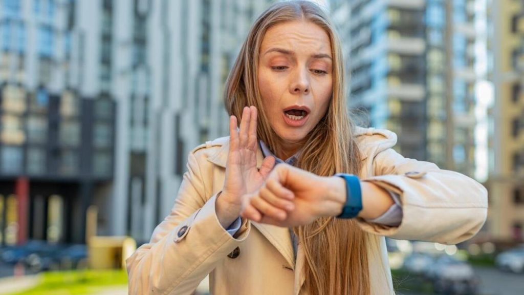 Žena na ulici prekvapene kontroluje čas na hodinkách, uvedomuje si meškanie