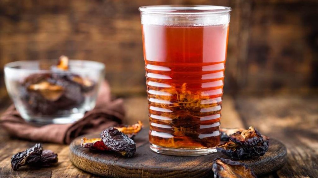 Pohár vody zo sušených sliviek s namočenými kúskami ovocia na drevenom stole