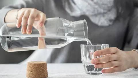 mladá žena prelieva vodu z fľaše do pohára