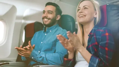 Usmiati cestujúci v lietadle tlieskajú po pristátí ako prejav radosti a vďaky pilotom.