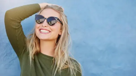 Usmiata žena v slnečných okuliaroch, symbolizujúca optimizmus a ľudí narodených pod šťastnou hviezdou.