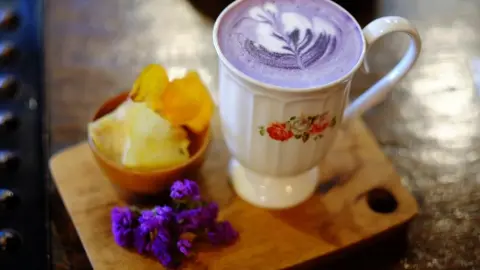 Goguma latte – kórejský nápoj z batata vo fialovej farbe, servírovaný v šálke s dekoráciou.
