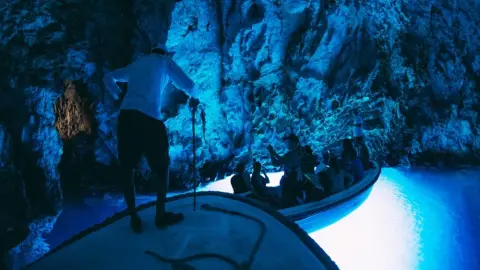 Turisti na člne vnútri Modrej jaskyne na chorvátskom ostrove Biševo, osvetlenej magickým modrým svetlom.