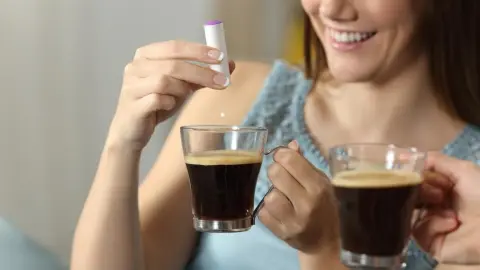 Žena s úsmevom pridáva sladidlo do šálky kávy