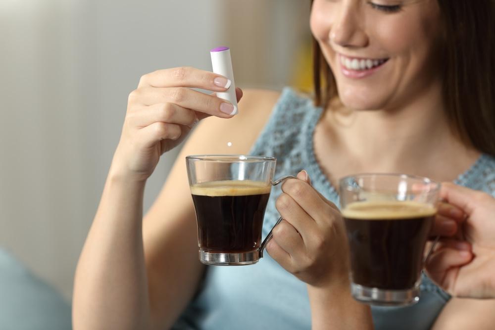 Žena s úsmevom pridáva sladidlo do šálky kávy