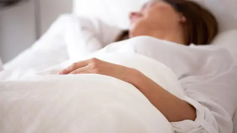 Žena odpočíva na chrbte v posteli – správna poloha spánku pomáha predchádzať vzniku spánkových vrások.