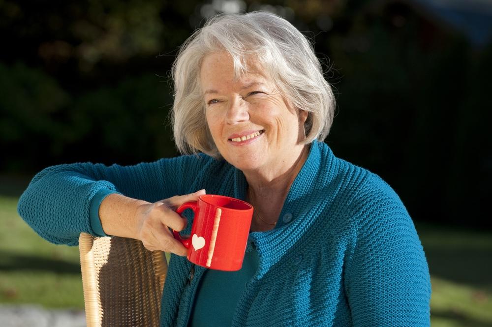 Šťastná staršia žena so šálkou kávy sedí na záhrade a usmieva sa