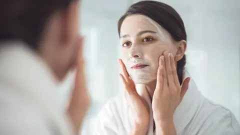Žena si pred zrkadlom nanáša domáci peeling zo sódy bikarbóny na pleť