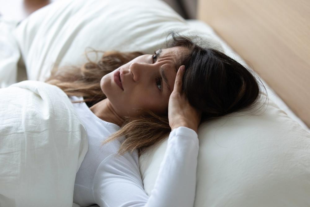 Žena leží v posteli a vyzerá vystresovane alebo bez nálady, s hlavou opretou o ruku – typický pondelkový pocit