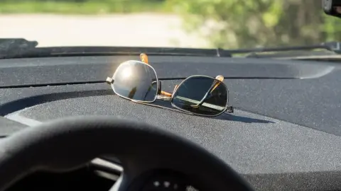 Slnečné okuliare položené na palubovej doske auta počas slnečného dňa