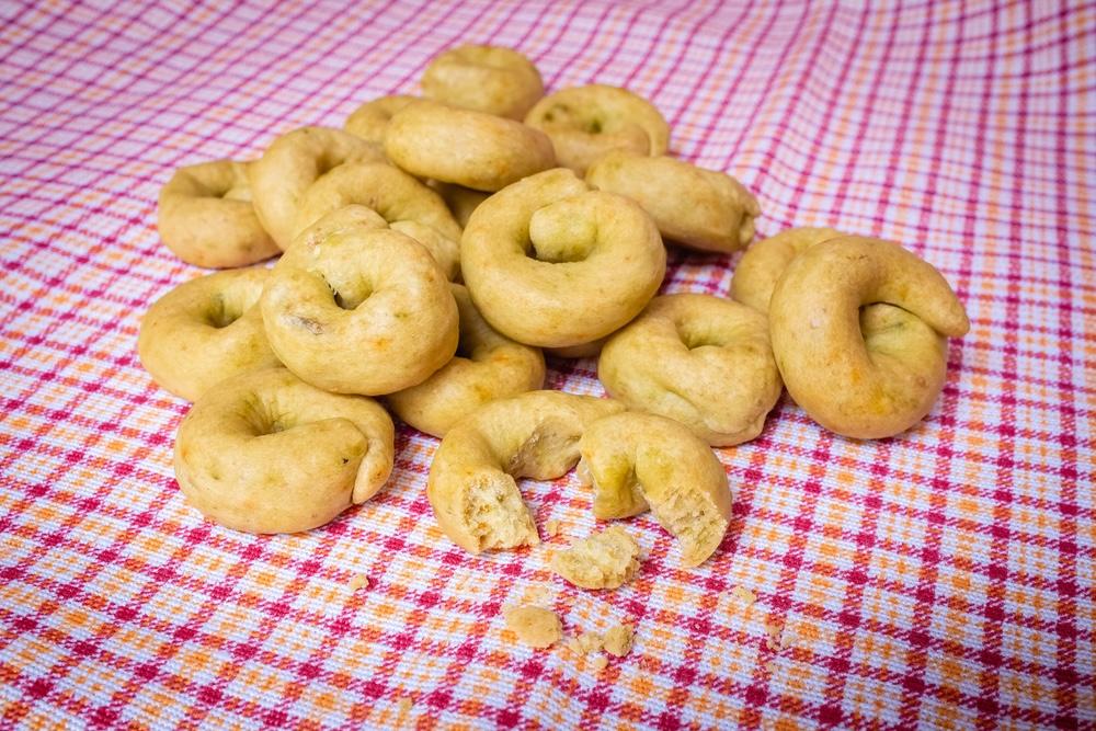 Hromada chrumkavých taralli na kockovanej servírke, niektoré z nich sú rozlomené.