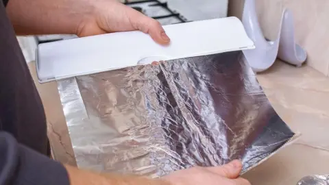 Muž odtrháva alobal z rolky v kuchyni na domáce použitie.