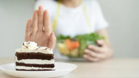 Žena odmieta kúsok čokoládovej torty a namiesto toho si vyberá misku so zeleninovým šalátom – rozhodnutie pre zdravší život bez cukru.