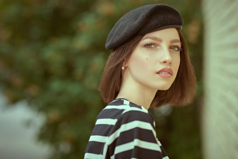 Mladá žena s francúzskym bobom a čiernym baretom, oblečená v pruhovanom tričku, pózuje vonku