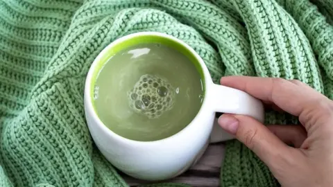 Šálka matcha čaju na zelenom pletenom svetri, držaná ženskou rukou