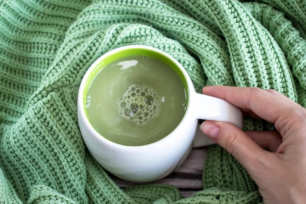 Šálka matcha čaju na zelenom pletenom svetri, držaná ženskou rukou
