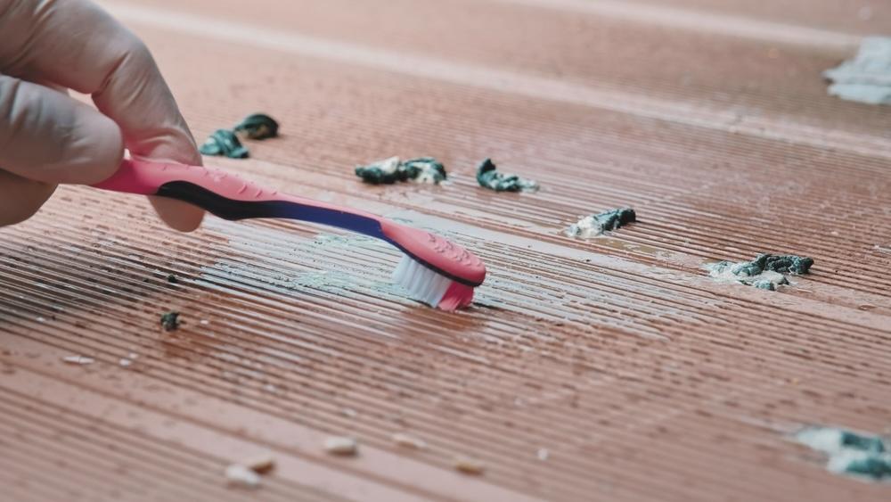 Ruka v rukavici čistí vtáčí trus z balkóna kefkou a vodou