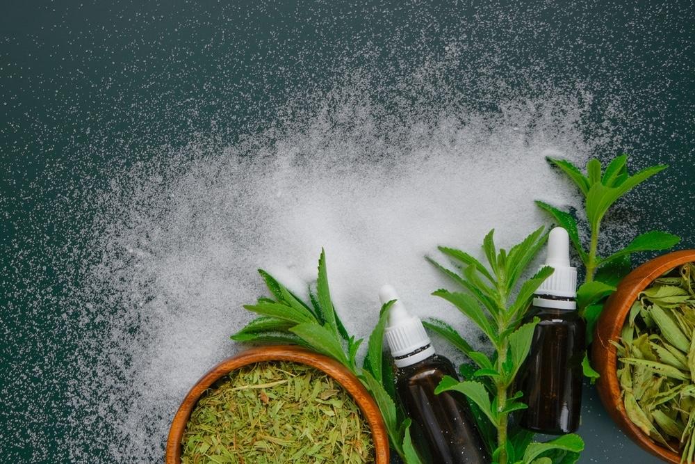 Listy rastliny stevia, kvapkadlá a sladký biely prášok na tmavom pozadí