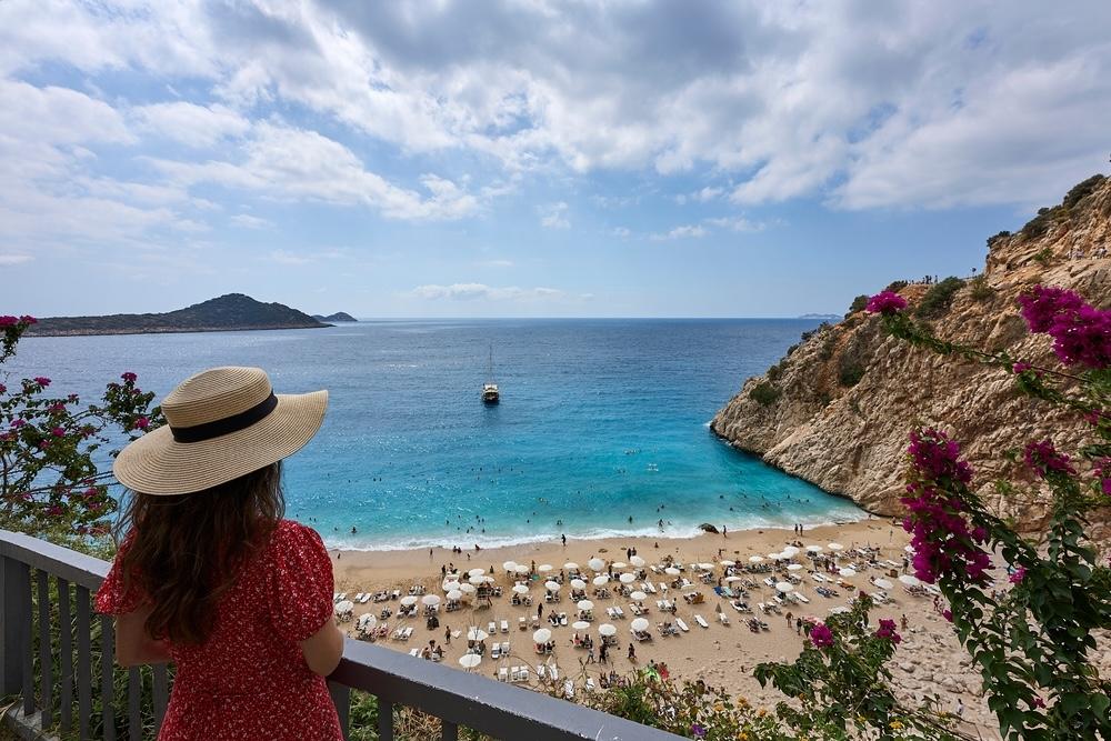 Žena v klobúku obdivuje tyrkysové more a piesočnatú pláž počas jesennej dovolenky v Turecku.