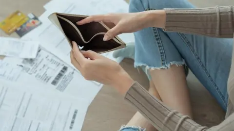 Žena sedí na podlahe s prázdnou peňaženkou v rukách, okolo nej účty a kreditné karty – symbol finančných problémov.