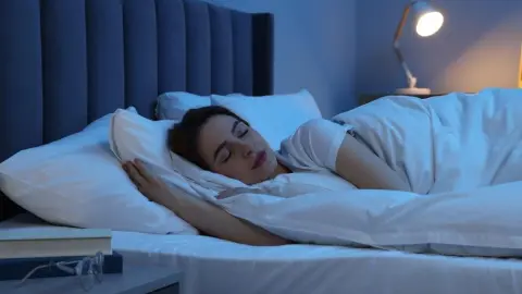 Žena spí v posteli so zapnutou nočnou lampou v spálni.