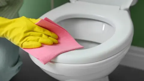 Čistenie toaletnej dosky ružovou handričkou v žltých gumených rukaviciach