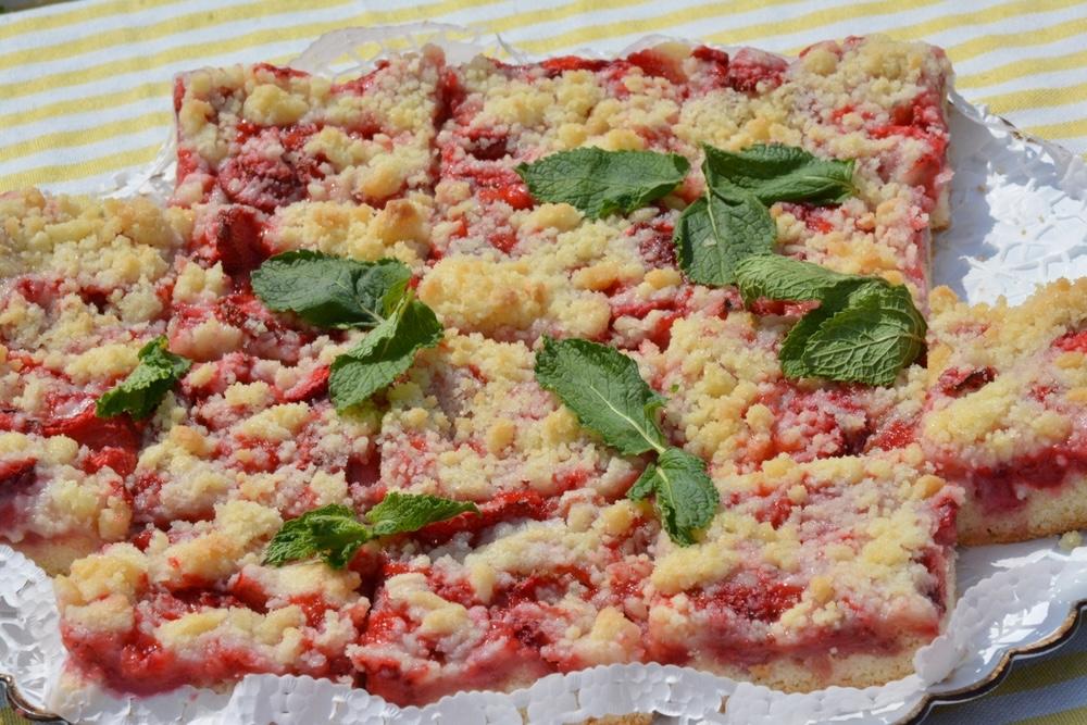 Domáci koláč s čerstvými jahodami a posýpkou, ozdobený lístkami mäty na bielom podnose.