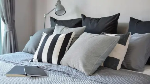Moderná spálňa s viacerými dekoratívnymi vankúšmi na posteli v odtieňoch sivej a čiernej.