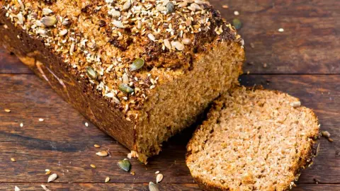 Domáci proteínový chlieb bez múky, posypaný semienkami, na drevenej doske