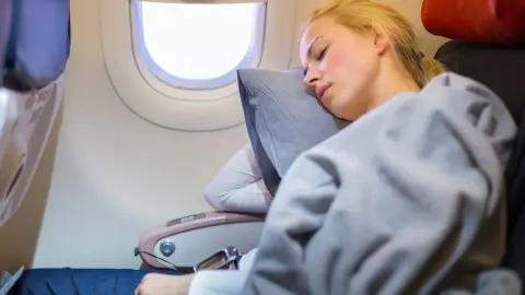 Žena pokojne spí v lietadle zabalená do deky počas letu