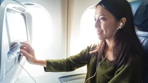 Žena sediaca v lietadle sleduje film na obrazovke v opierke sedadla počas letu.